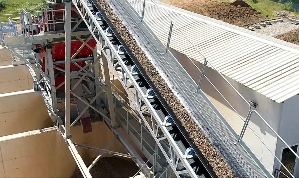 Inclined conveyor carrying gravel up to a J Mould screening plant above concrete storage bays