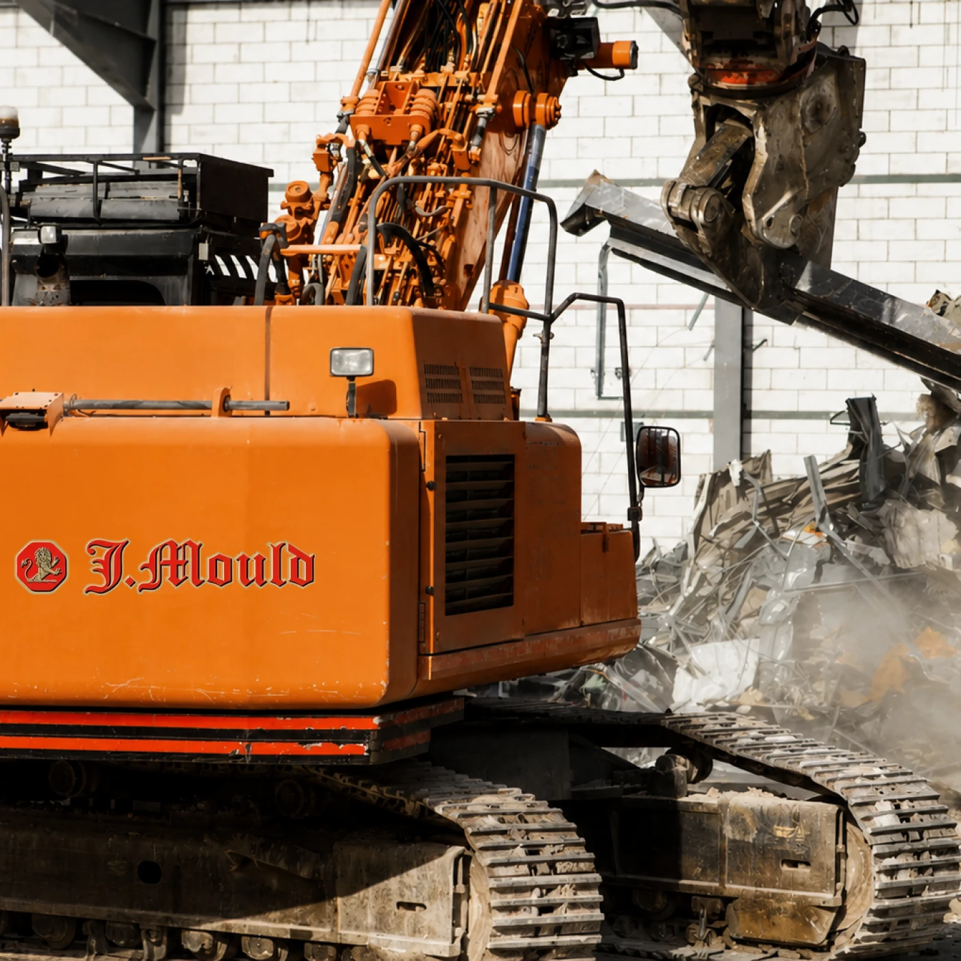 Orange J Mould demolition excavator with a crusher attachment pulling down steel beams inside a building