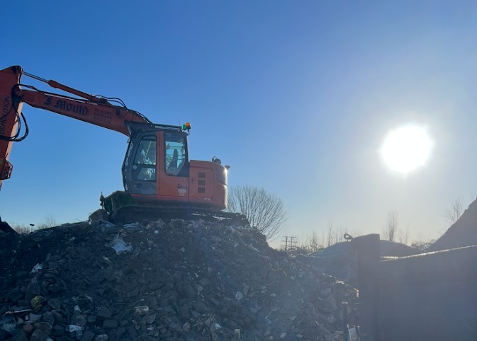 Orange J Mould excavator on top of a heap of demolition rubble against a low winter sun
