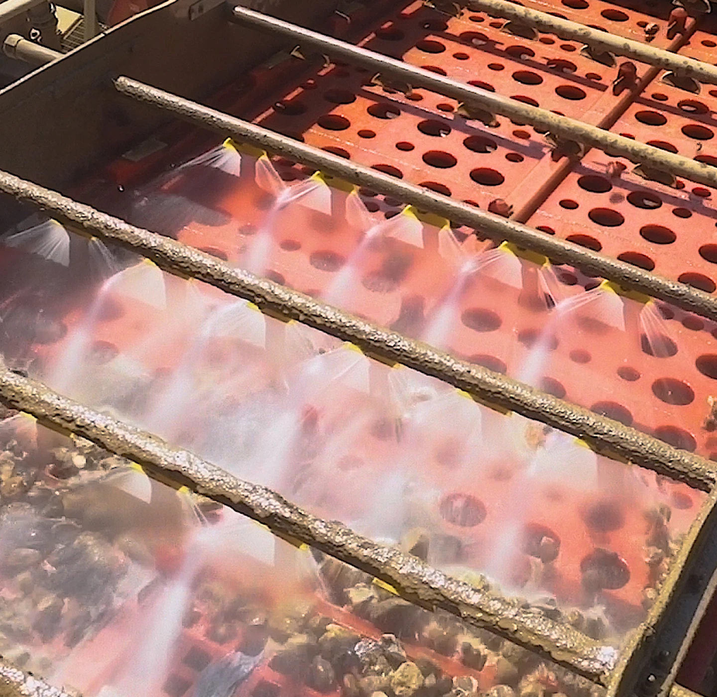 Water spray bars rinsing gravel on the red perforated deck of a J Mould aggregate washing screen