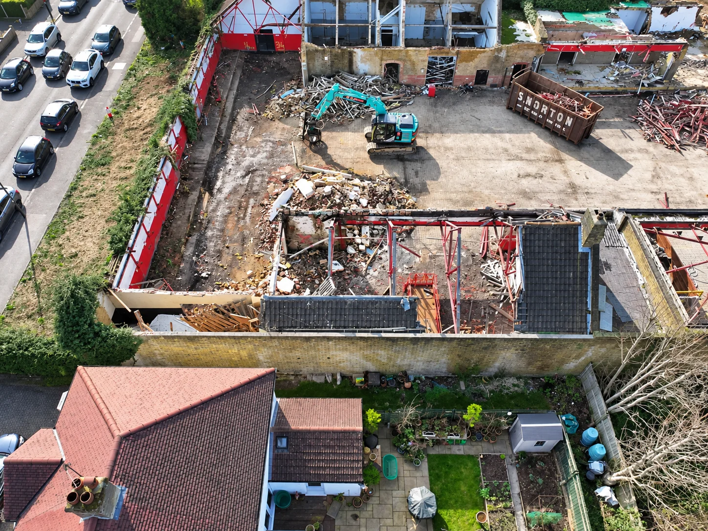 Aerial view of a demolition site with an excavator and a skip labelled S.Norton