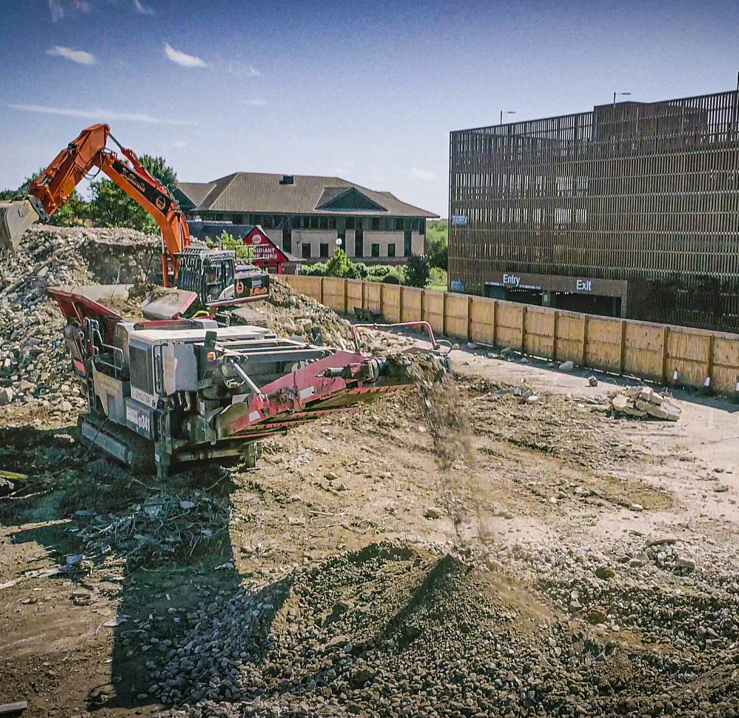 Mobile crusher fed by an orange J Mould excavator, turning demolition rubble into crushed aggregate