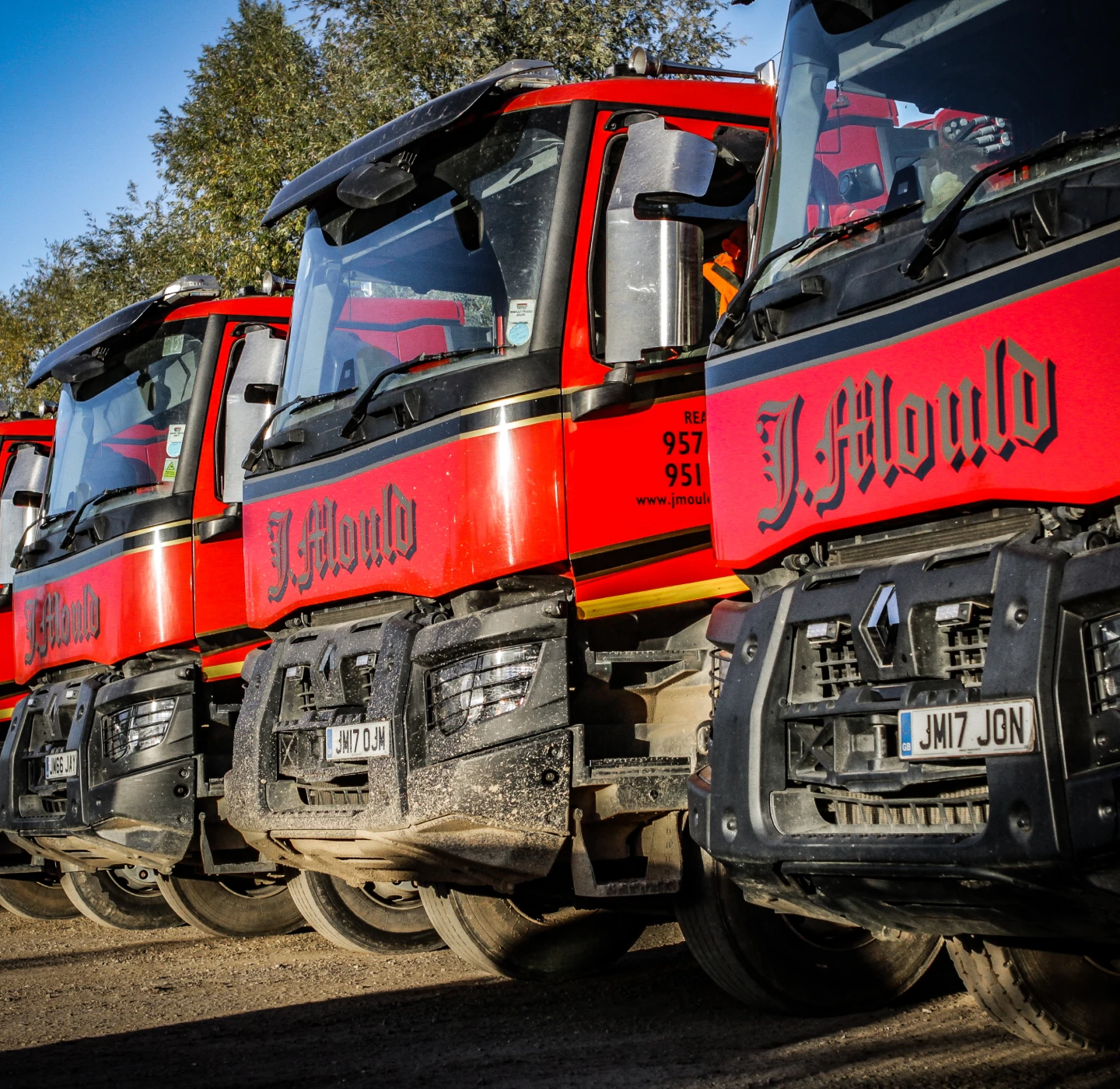 Row of red J Mould Renault lorries parked nose to tail, the J Mould name across each cab front