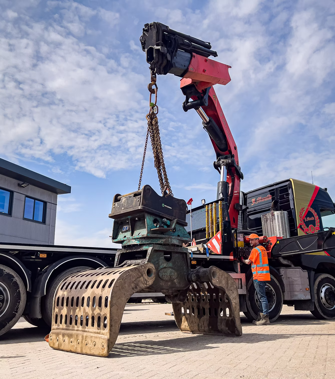 J Mould lorry-mounted crane lifting an excavator sorting grab on chains while an operator in hi-vis works the controls