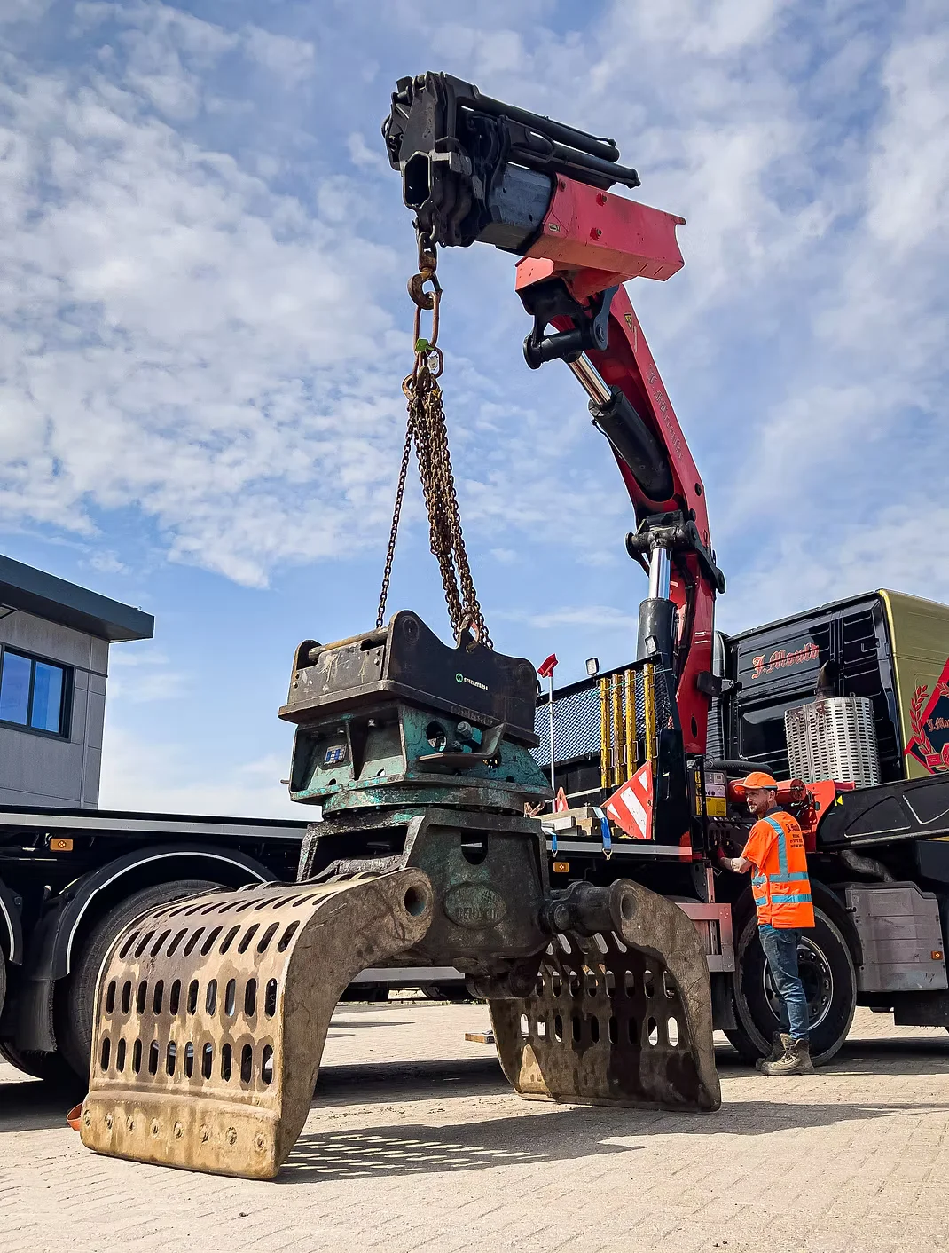 J Mould lorry-mounted HIAB crane lifting a demolition sorting grab on chains, with an operator in hi-vis