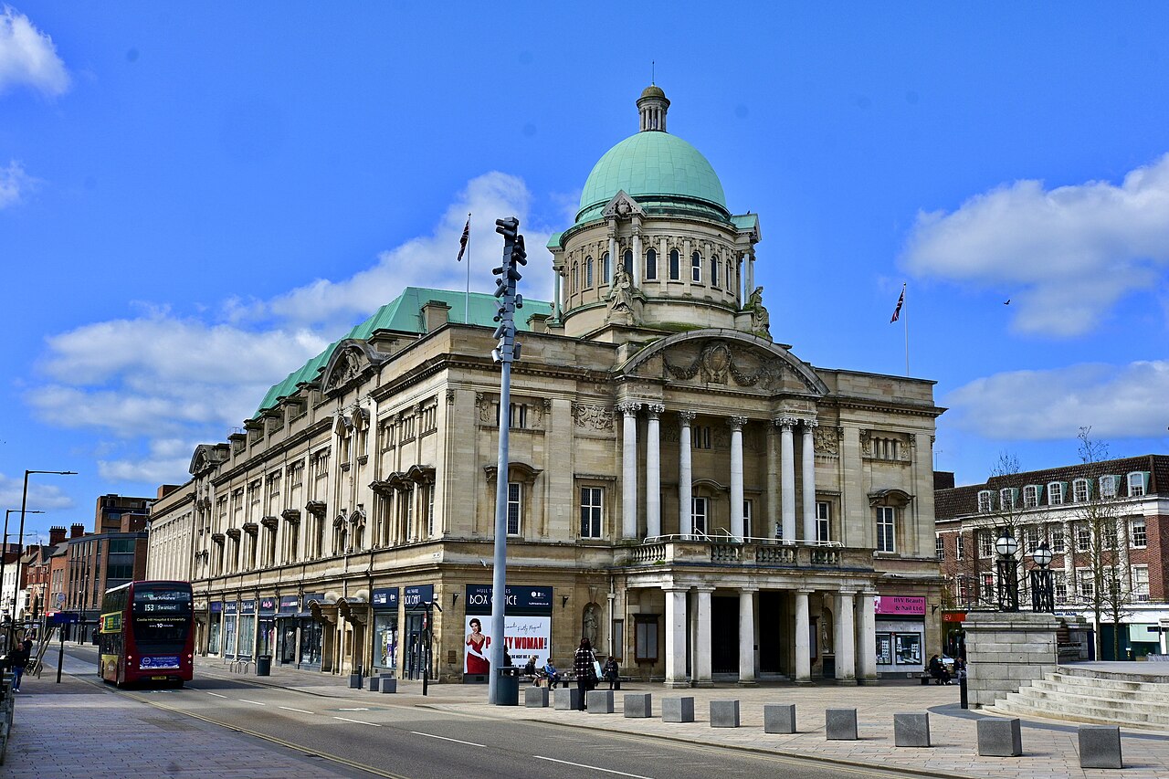 Hull City Hall with its green dome beside a red double-decker bus, a city J Mould covers for demolition