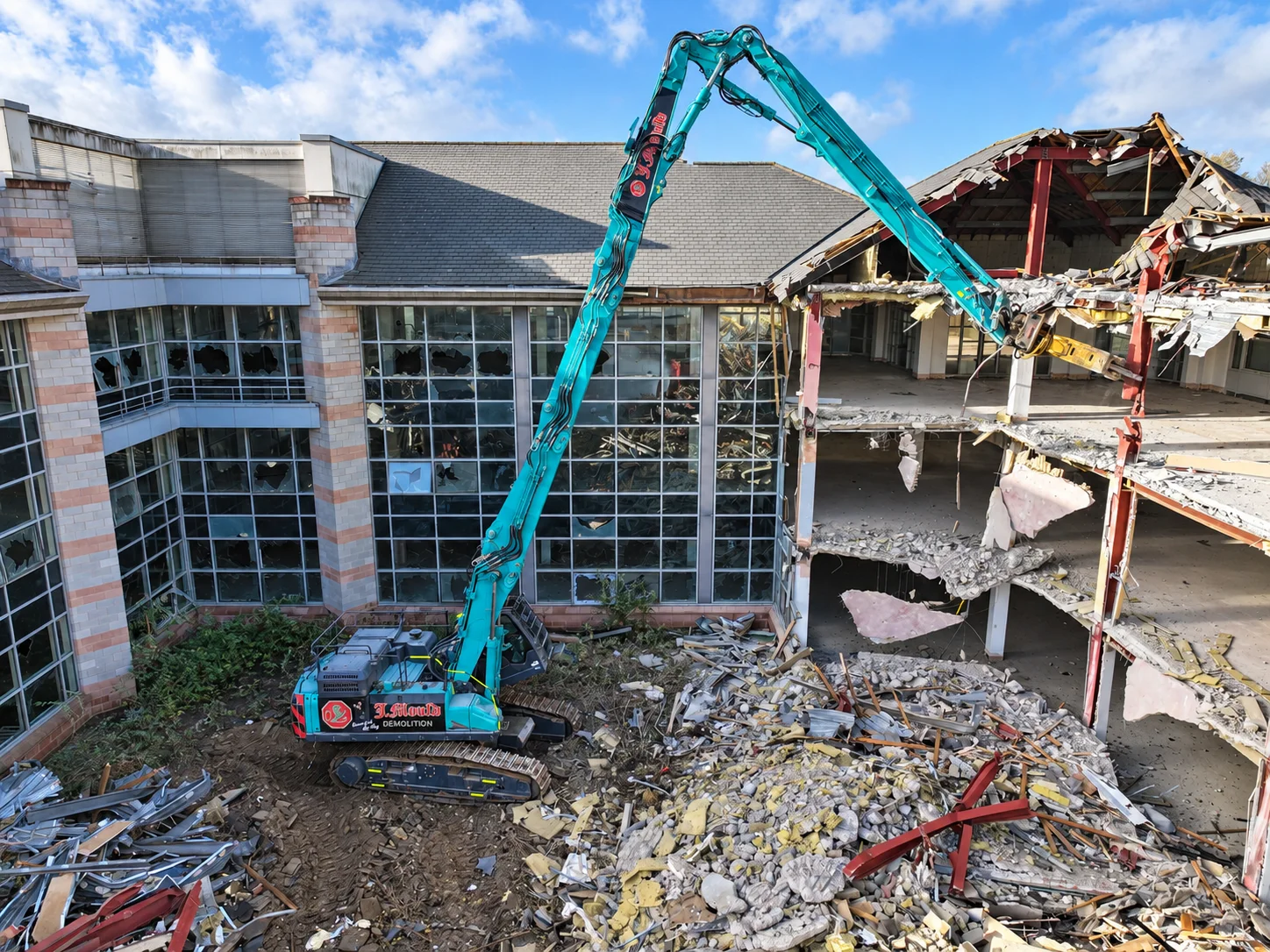 Teal J Mould Demolition high-reach excavator taking down a glass-fronted office building, its floors exposed