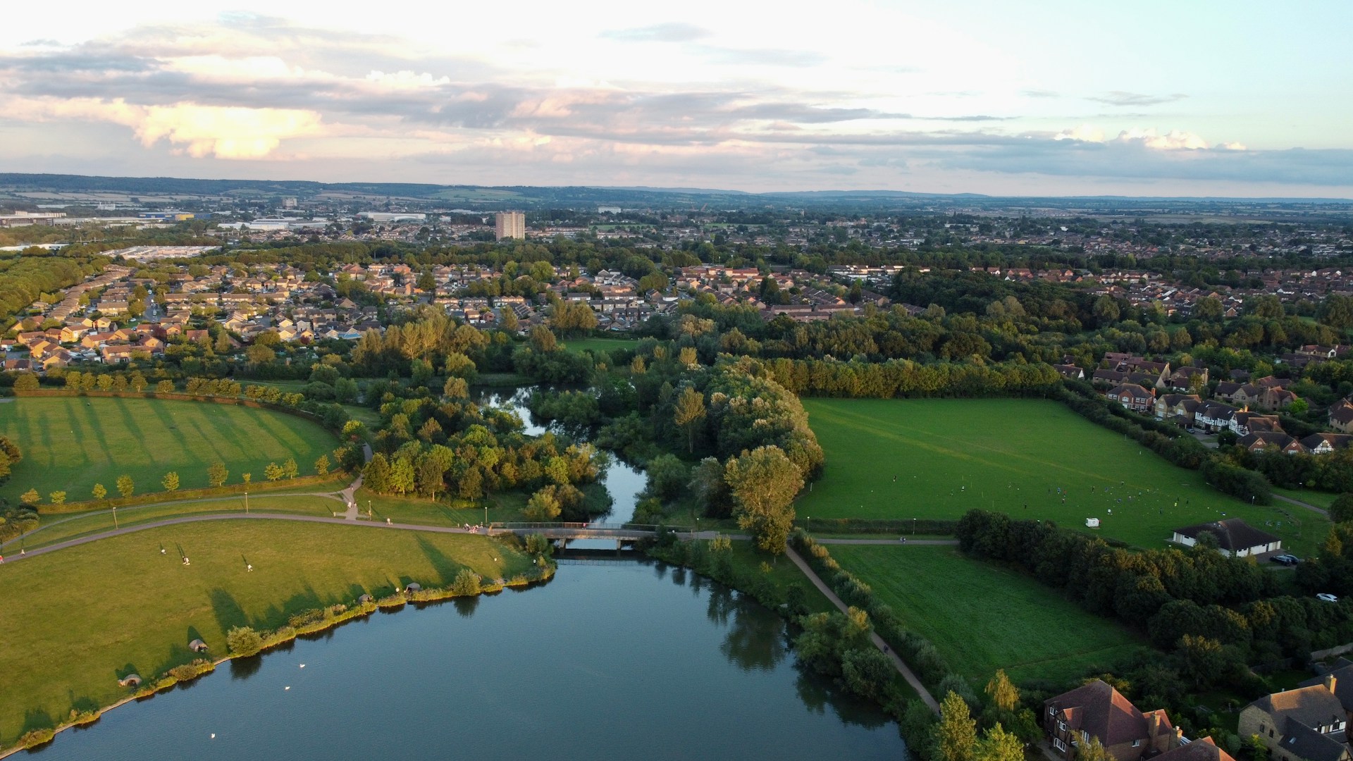 Aerial view of a lake, footbridge and parkland with housing beyond, an area J Mould covers for demolition