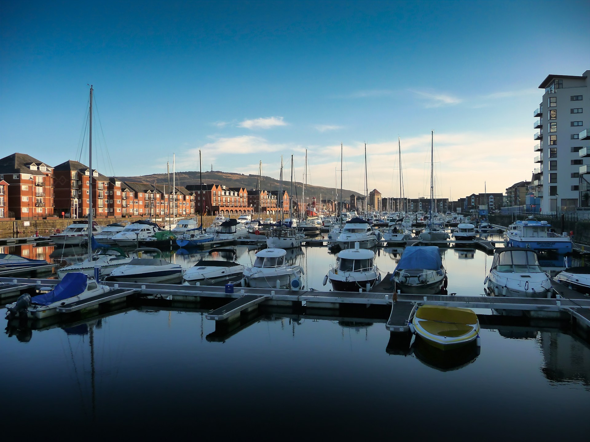 Yachts moored in a marina lined with red-brick flats, an area J Mould covers for demolition