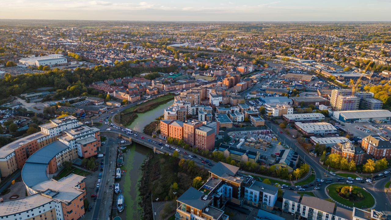 Aerial view of a town at sunset with a river, moored boats, a road bridge and blocks of flats
