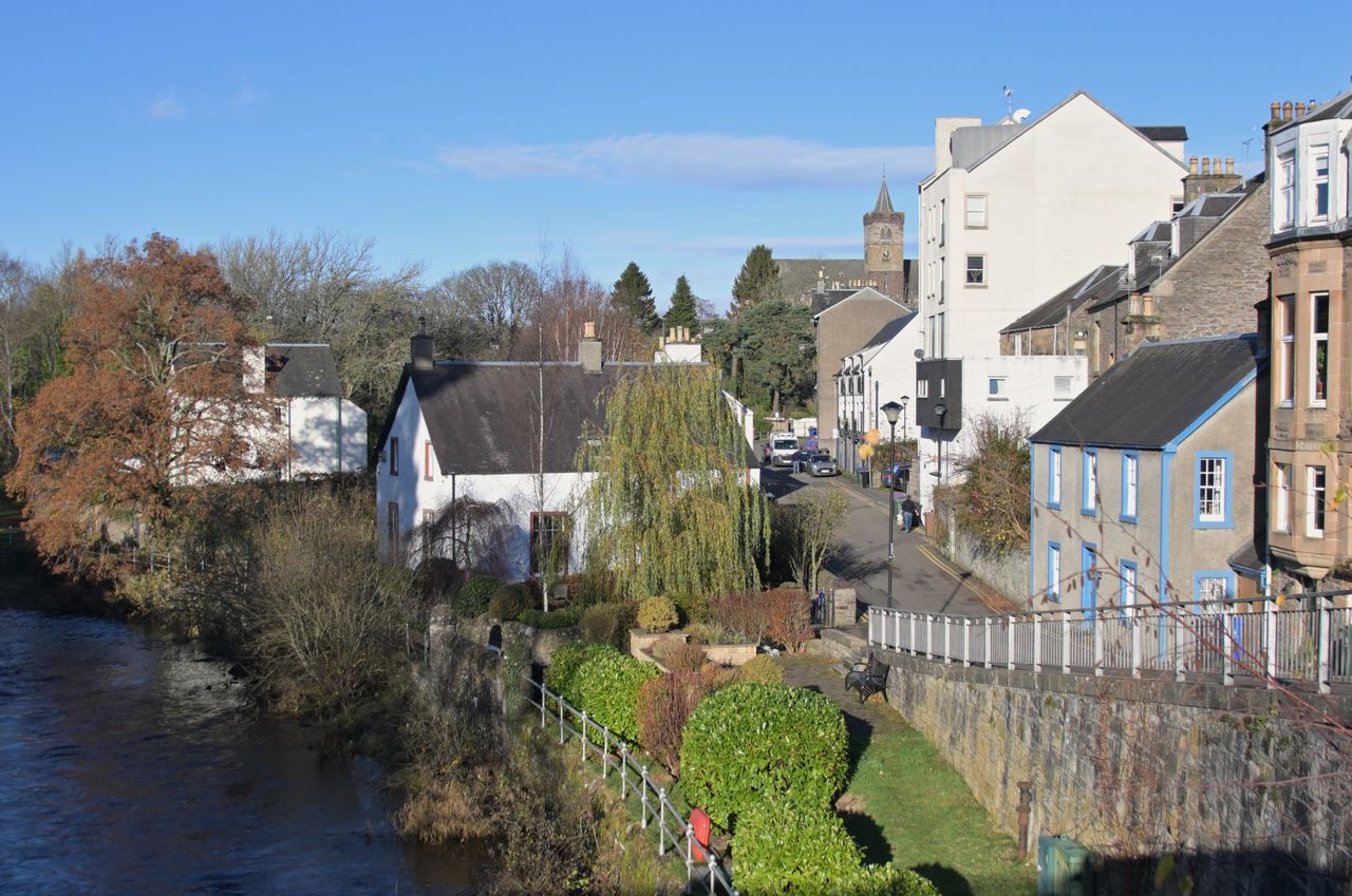 Riverside lane of white and stone houses with a weeping willow and a church tower beyond