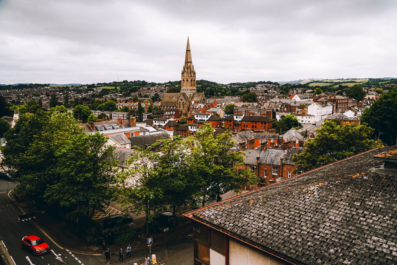 Town rooftops with a Victorian church spire and green hills, an area J Mould covers for demolition