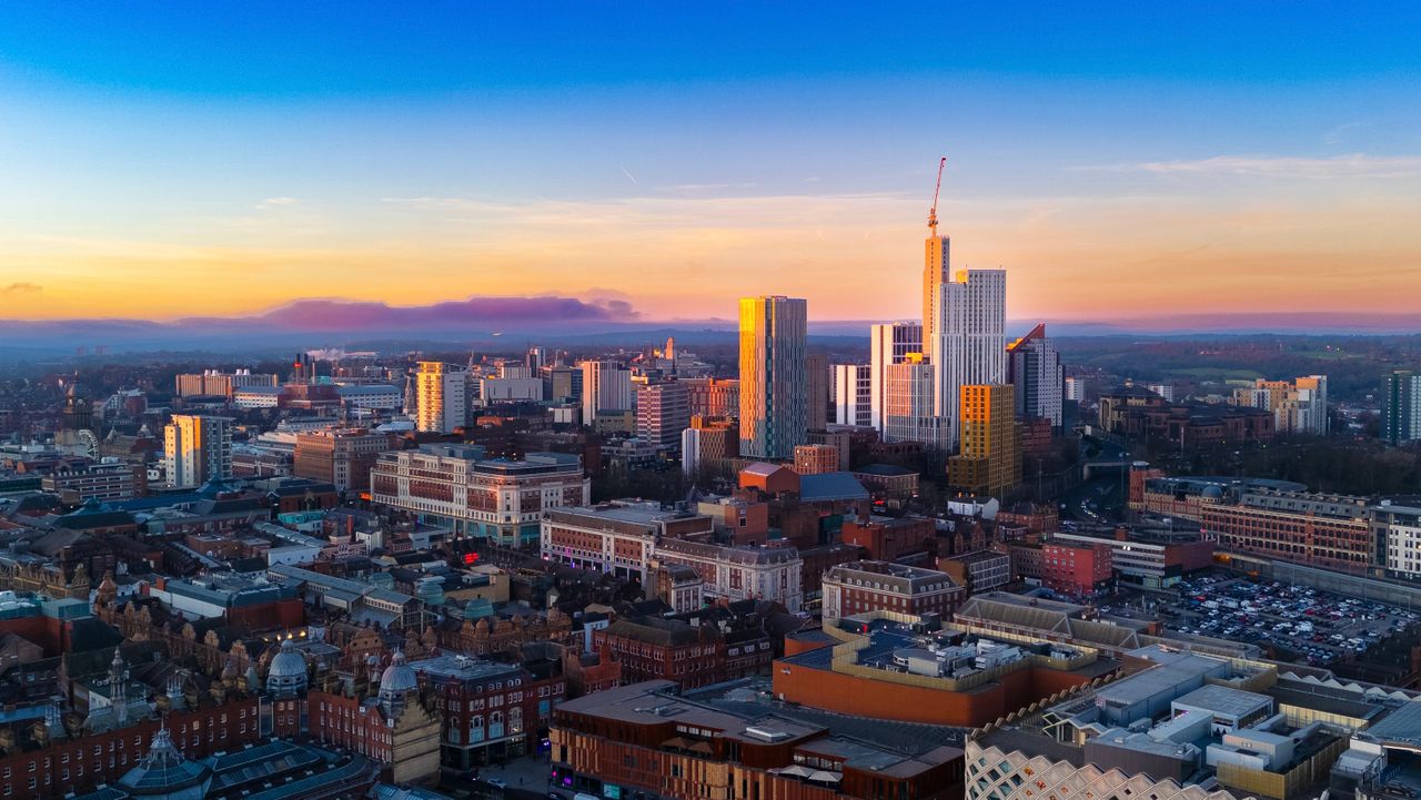 City centre skyline at sunset with high-rise towers, a tower crane and Victorian rooftops