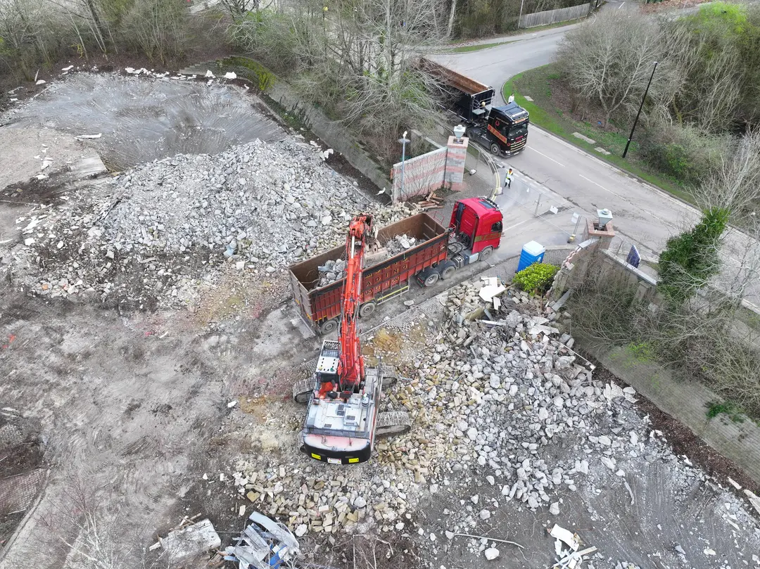 Aerial view of a red J Mould grab lorry loading rubble at a rural clearance site