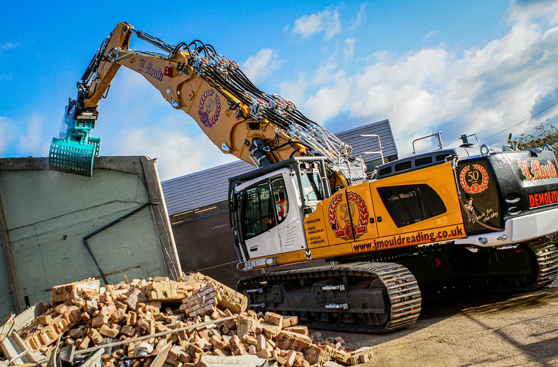 Yellow J Mould demolition excavator with a 50 years crest using a sorting grab beside a pile of bricks
